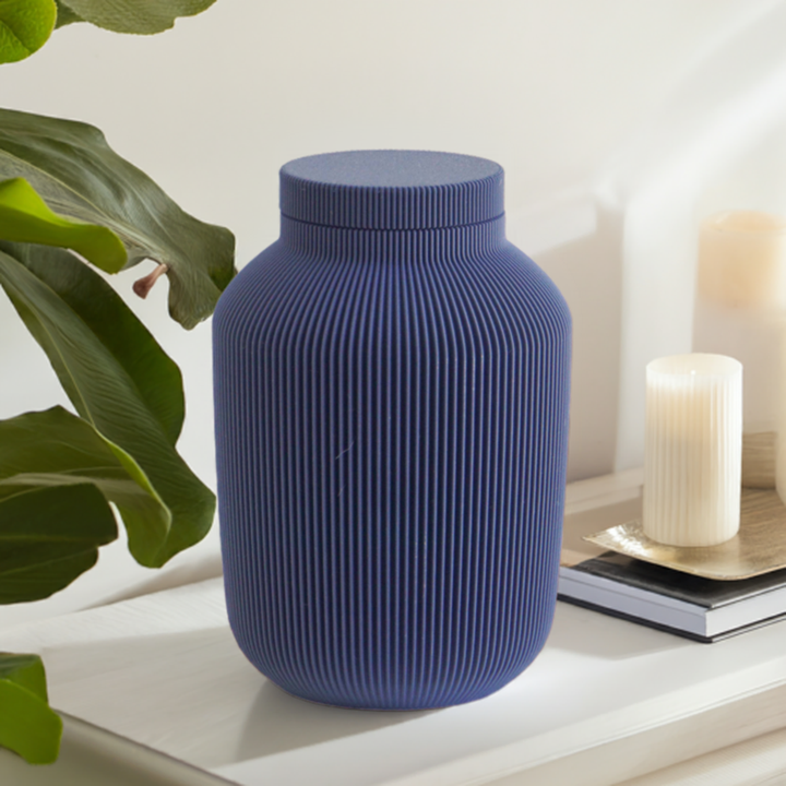 Willow cremation urn in navy with modern vertical sculpted texture, displayed with greenery and a candle.