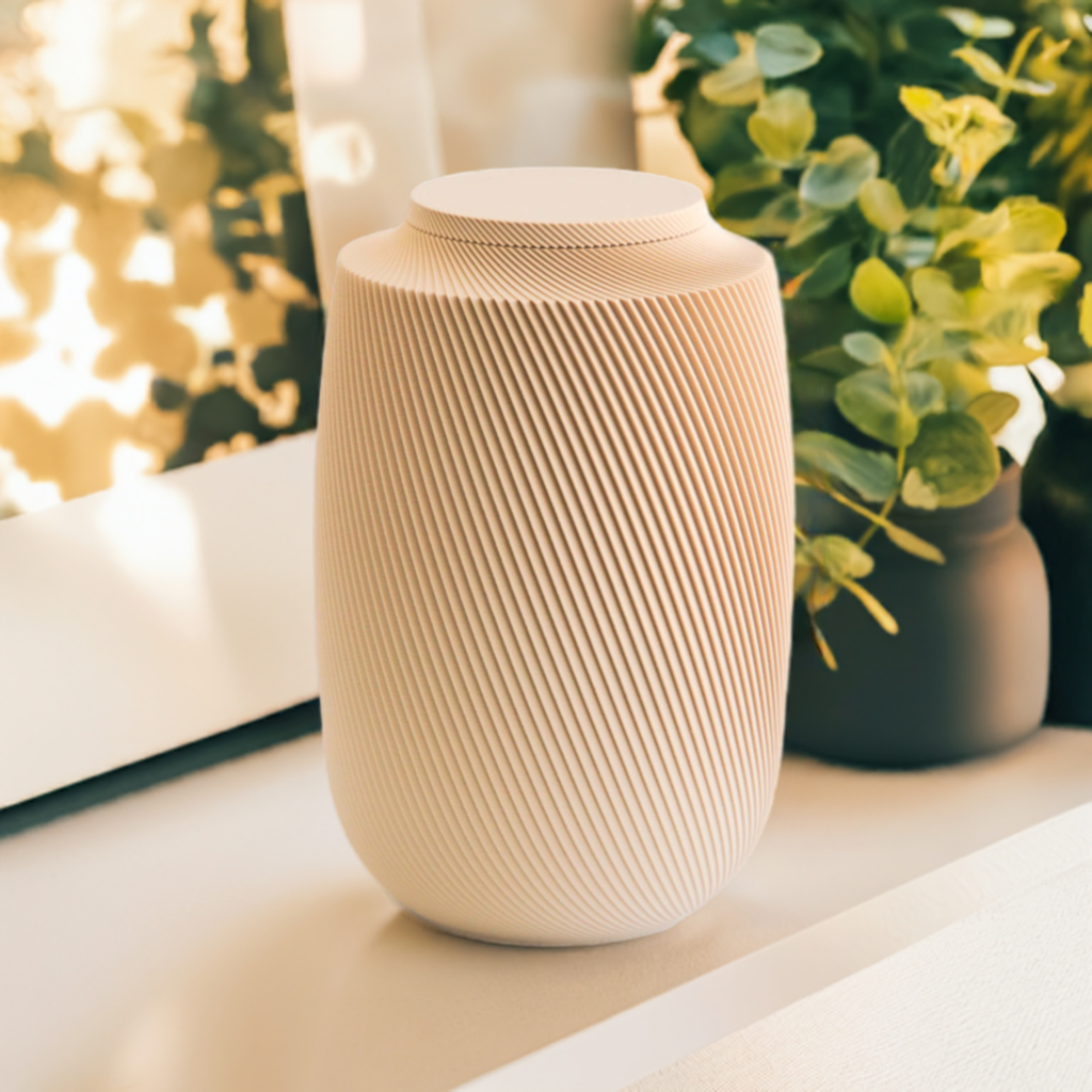 Warm tan Aspen cremation urn with modern spiral sculpted design, styled with greenery in soft natural light.