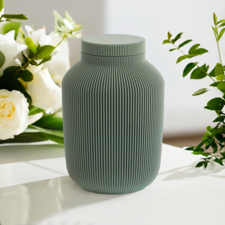 Willow cremation urn in green with modern vertical sculpted texture, displayed with white flowers and greenery.