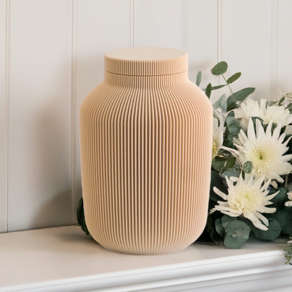 Willow cremation urn in tan with modern vertical sculpted texture, displayed with white flowers and greenery.