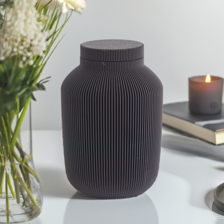 Willow cremation urn in black with modern vertical sculpted texture, displayed with flowers and a lit candle.