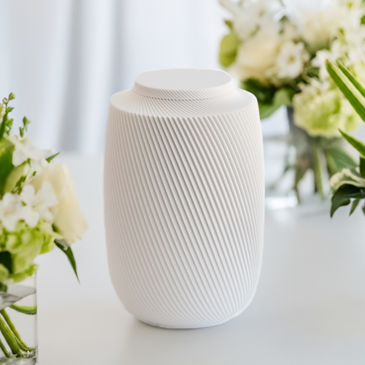 Aspen cremation urn in white with modern sculpted texture, displayed with white floral arrangements.