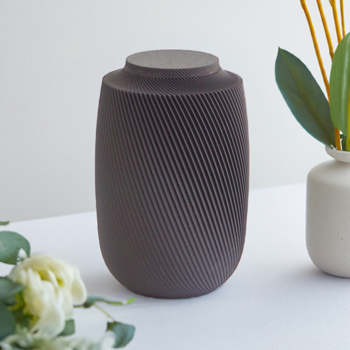 Aspen cremation urn in black with modern sculpted texture, displayed on a white surface with greenery.