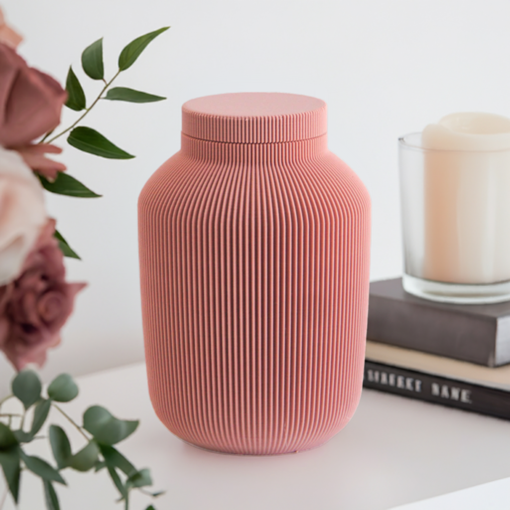Willow cremation urn in pink with modern vertical sculpted texture, displayed with books and a candle.