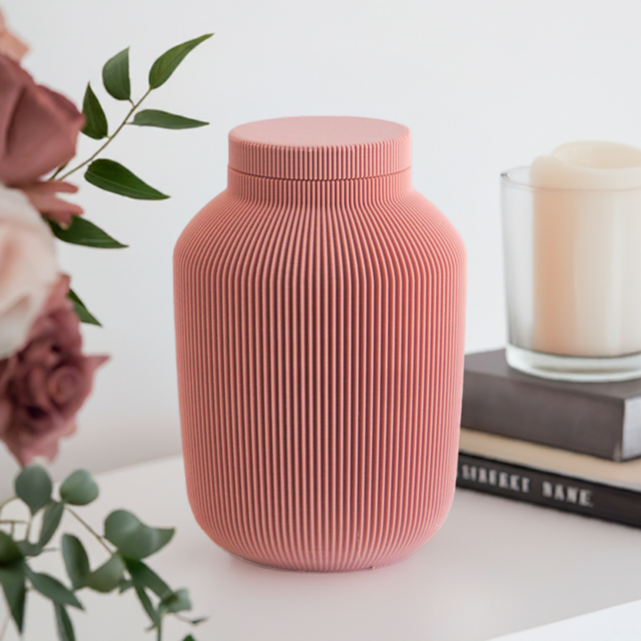 Willow cremation urn in pink with modern vertical sculpted texture, displayed with books and a candle.