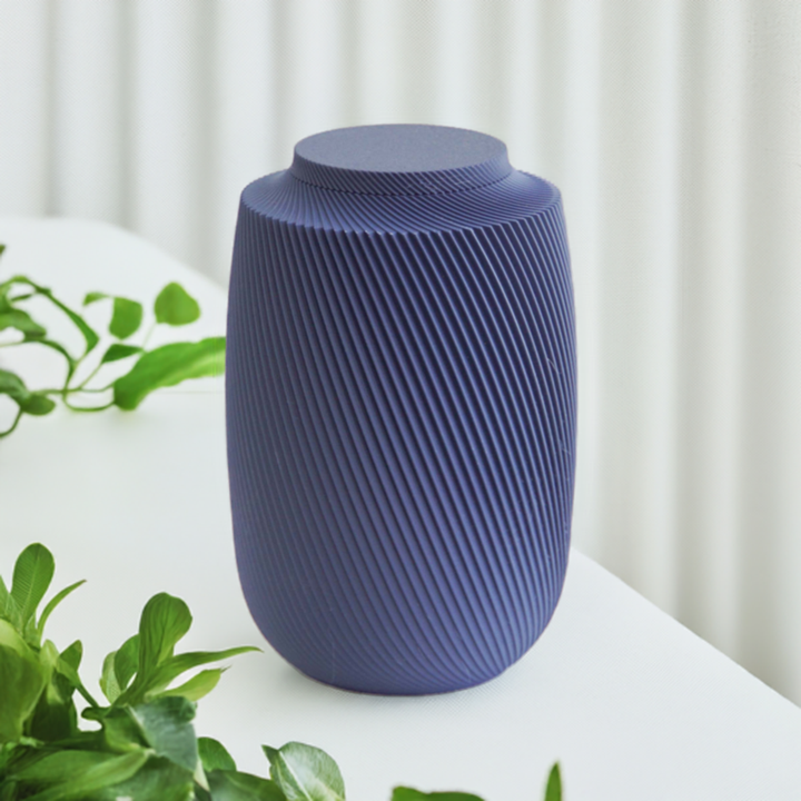 Aspen cremation urn in navy with modern sculpted texture, displayed on a white surface with greenery.